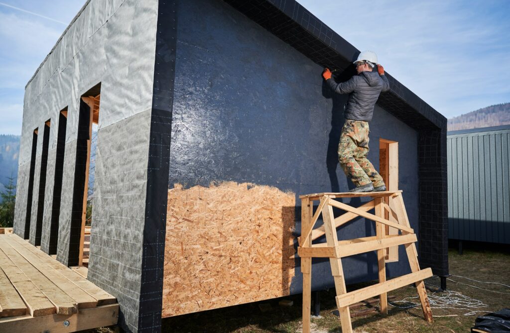 Male painter using paint roller, doing exterior paint work while building wooden frame house.