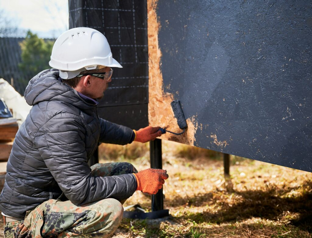 Male painter using paint roller, doing exterior paint work while building wooden frame house.